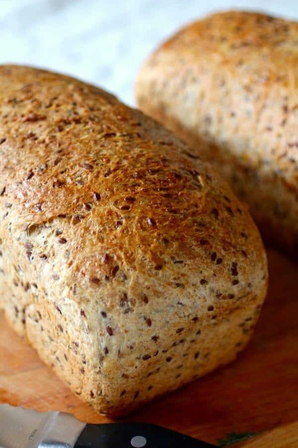 A loaf of multigrain flaxseed bread on a cutting board.