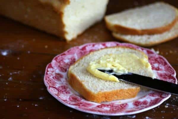 A slice of white bread being spread with butter.