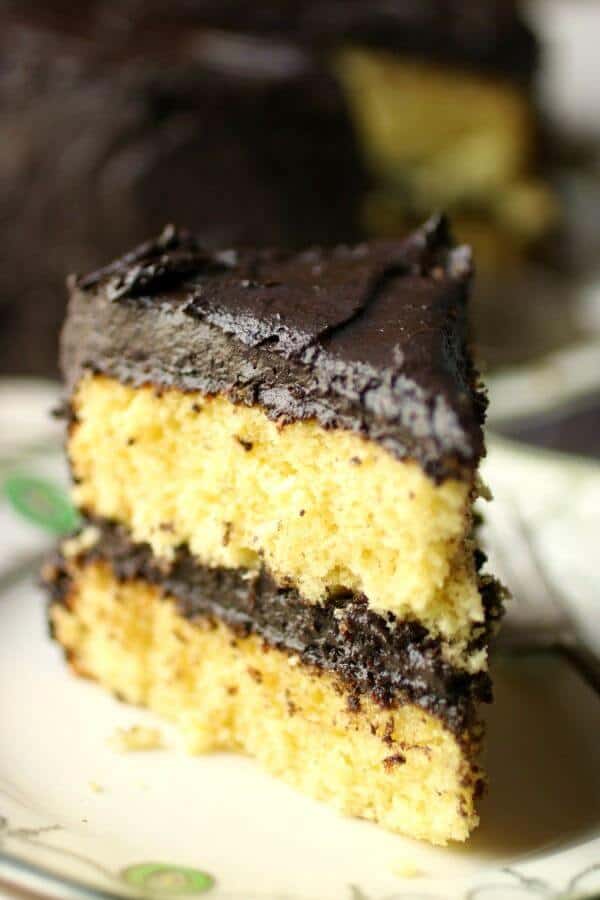 Close up of a yellow layer cake slice with fudge frosting on the top and sides as well as between the layers.