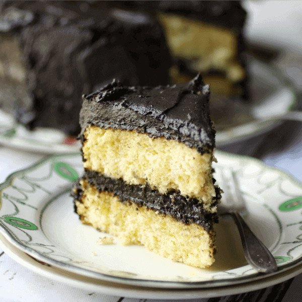 A slice of yellow layer cake with fudge frosting.