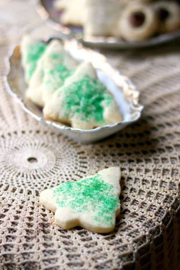 The best rolled sugar cookies recipe ever! So easy! Make sugar cookies that keep their shape plus tips and tricks to make them even better. From RestlessChipotle.com #sugarcookiesrecipe #rolledsugarcookies #bestsugarcookies One sugar cookie is on a lace covered table while the rest of the best sugar cookies recipe with green sugar are in an antique dish