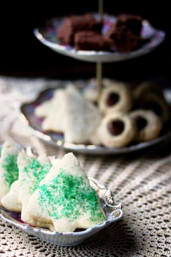 The best rolled sugar cookies recipe ever! So easy! Make sugar cookies that keep their shape plus tips and tricks to make them even better. From RestlessChipotle.com #sugarcookiesrecipe #rolledsugarcookies #bestsugarcookies Sugar cookies sprinkled with green sugar are on a lace covered table along with an antique tiered plate of cookies. Best rolled sugar cookies recipe vertical image 4