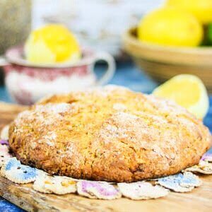 Round loaf of Irish soda bread on a doily with lemons in the background.