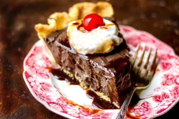 Slice of chocolate pie topped with whipped cream and a cherry, on a red transferware plate - feature image