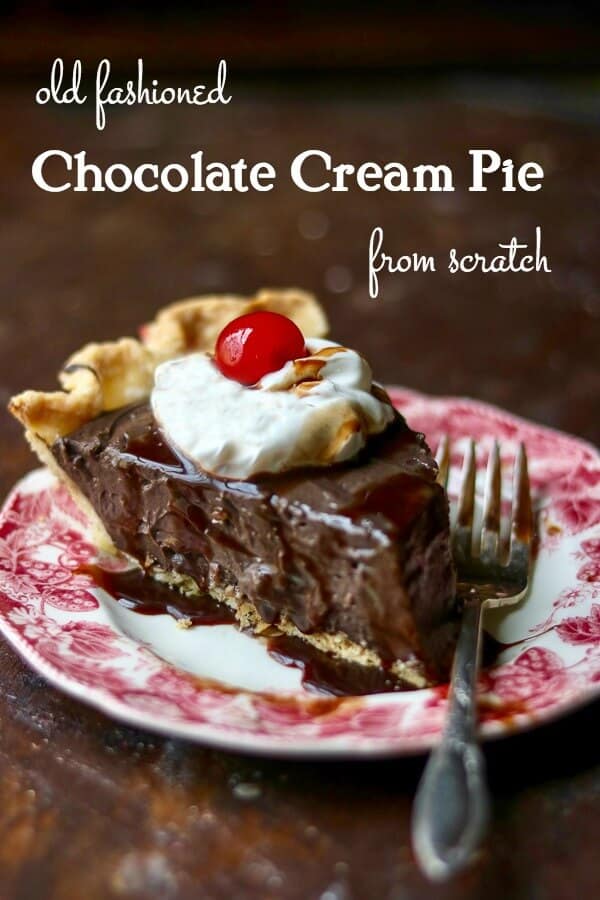 Thick slice of chocolate cream pie with whipped cream and a cherry on top. The pie is on a red transferware plate. Title image.