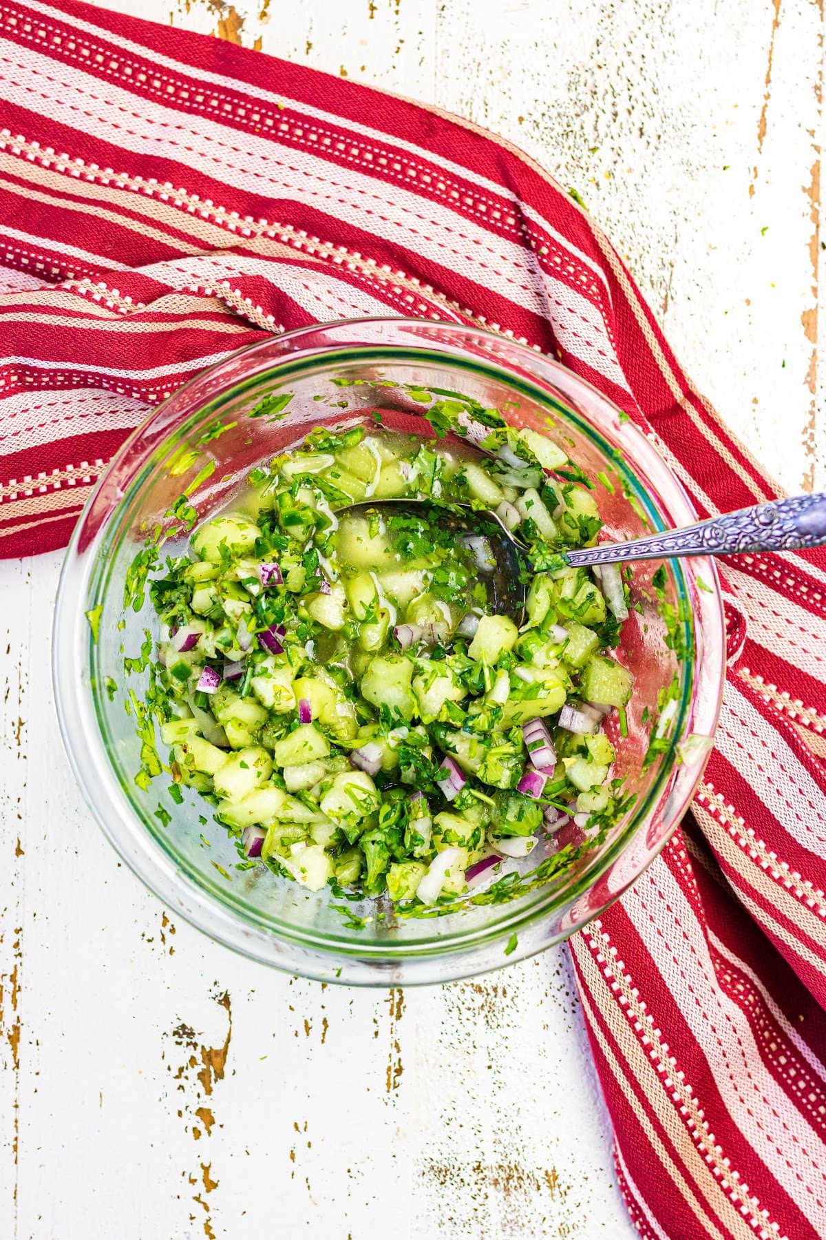 Overhead view of green honeydew salsa on a white table.