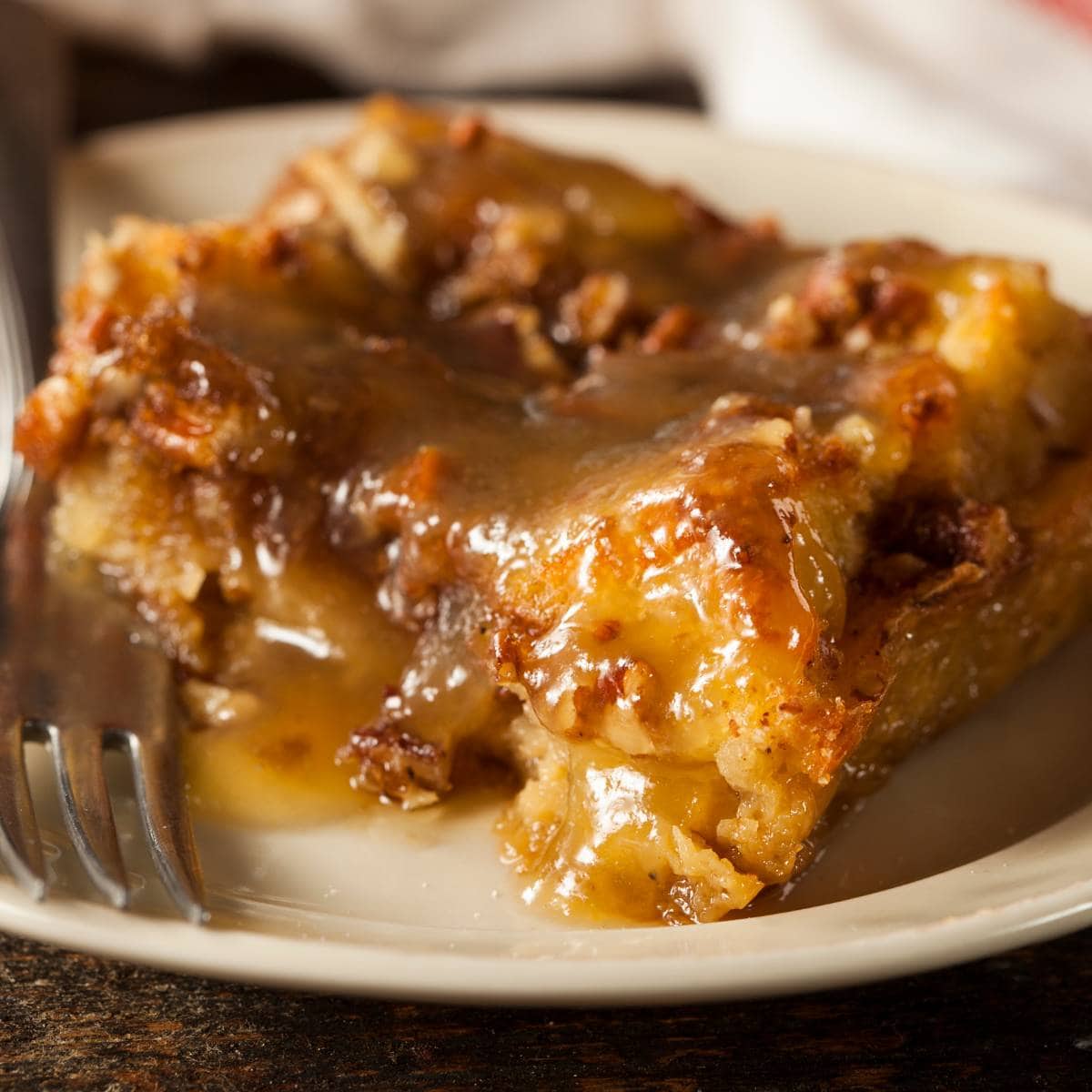 A square of bread pudding on a plate with caramel sauce.