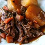 Close up of the pot roast with carrots, potatoes, and more on a vintage white and green plate.