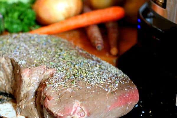 A piece of raw beef pot roast seasoned with herbs, salt, and pepper.