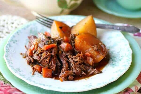 A serving of the tender, perfect pot roast on an antique jadite plate with a silver fork in the background.