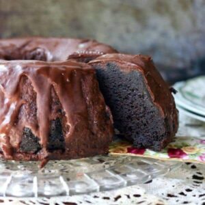 Slice of black lager chocolate cake on a flowered china cake server with a lace tablecloth underneath.