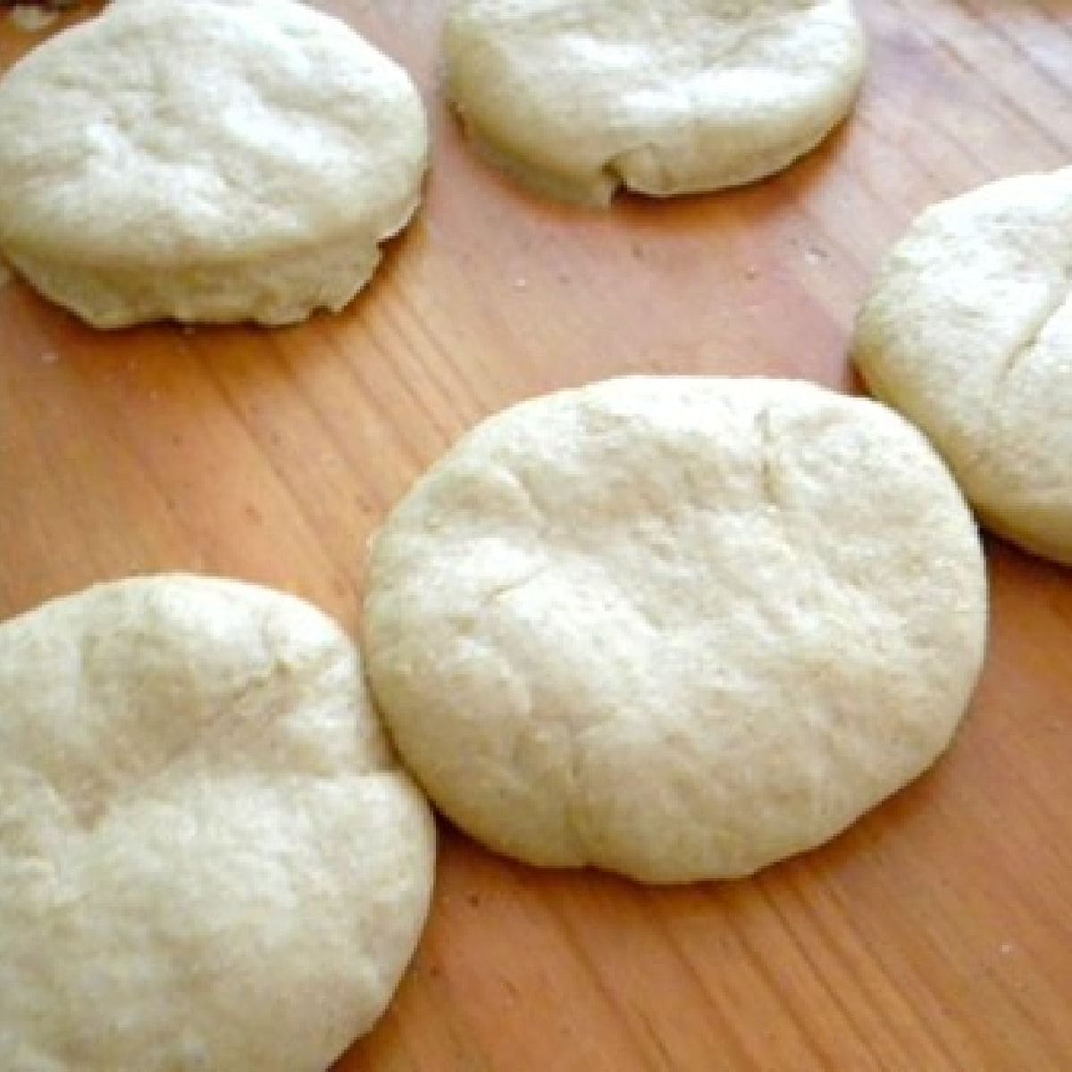 Unbaked hamburger buns on a wooden counter.