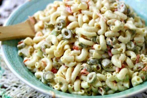 Creamy macaroni salad in a green bowl with a wooden spoon.
