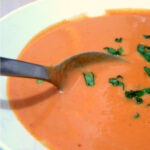 A bowl of cream of tomato soup with chopped basil on top.