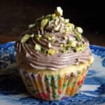 Vanilla cupcake with chocolate frosting and chopped pistachio nuts on top.