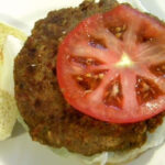 Closeup of a cooked veggie burger with a sliced tomato on top.