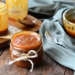 Jar of caramel sauce on a wood table.