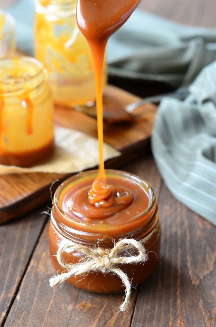 Spoon dribbling caramel sauce into a jar.