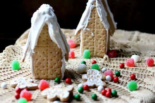 two gingerbread houses with cookies and red and green candy on a lace covered table