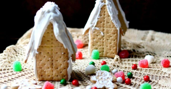 two gingerbread houses on a table await decoration. Green and red candy is strewn around