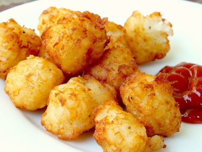 homemade tater tots on a white plate with catsup on the side.