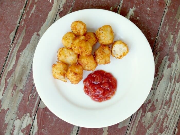 A pile of homemade tater tots on plate with a puddle of catsup next to it.