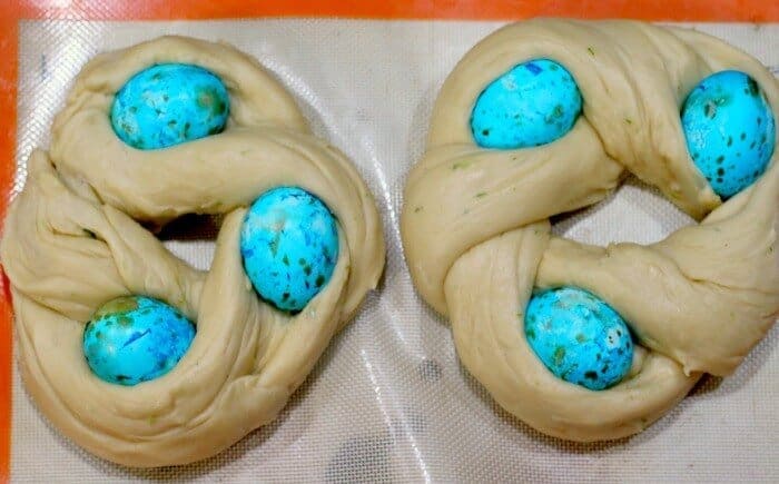 Two braided wreaths of unbaked Easter egg bread rising on the baking sheet.