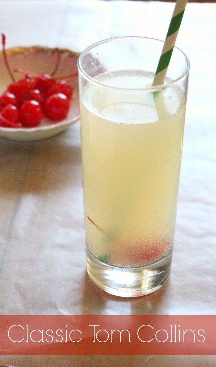 A tom collins cocktail in a highball glass with cherries in the background.