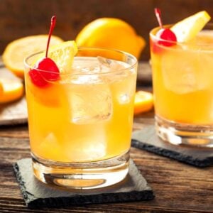 Closeup of two whiskey cocktails garnished with cherries.