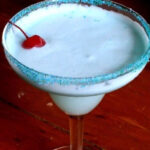 A closeup of a creamy blue cocktail with a cherry on top.