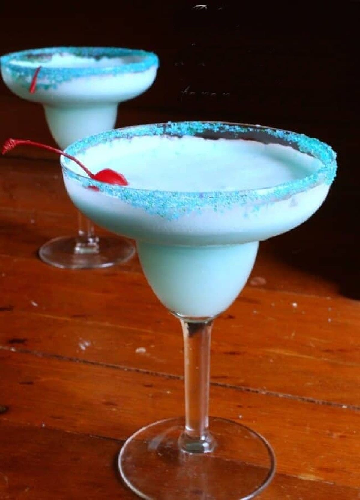 Two stemmed glasses with this light blue cocktail inside.