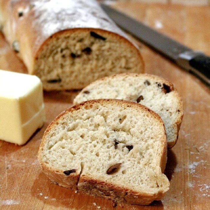 A sliced loaf of olive bread on a breadboard.