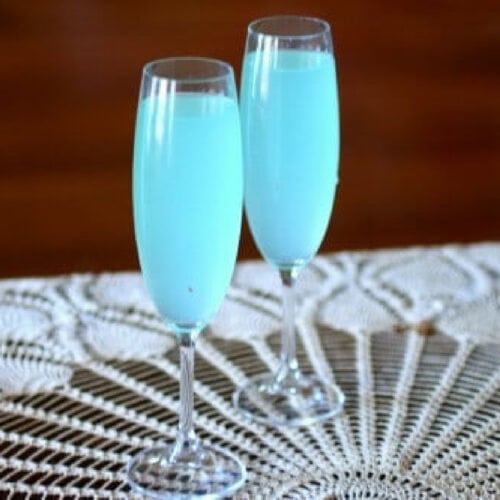 Two champagne glasses with sparkling light blue cocktail in them.