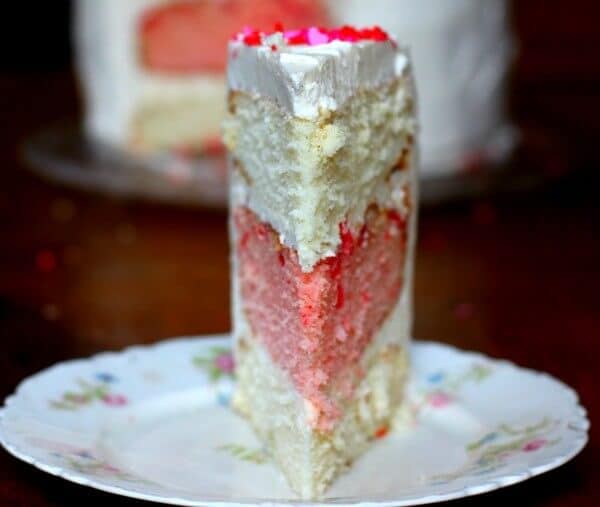 Sliced cake showing white almond cake layers with a layer of pink cherry cake in between them.