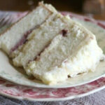 A slice of triple-layer white coconut cake with red raspberry jam between the layers.
