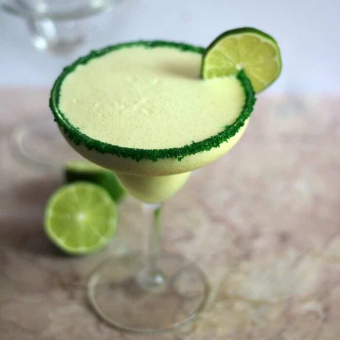A creamy, light green cocktail garnished with lime in a margarita glass with a green sugared rim.