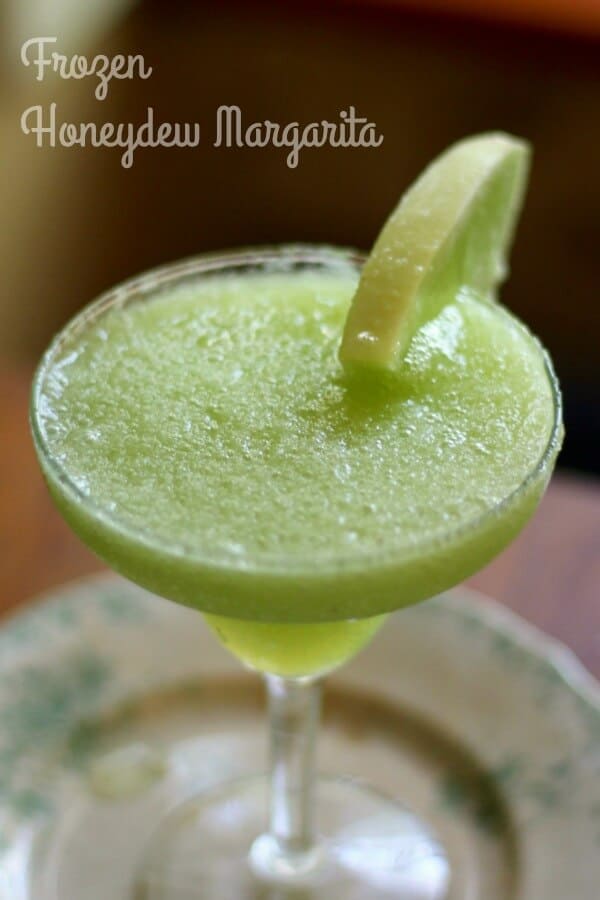 light green frozen honeydew margarita in a glass with a lime garnish.