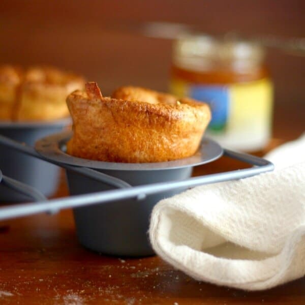 Closeup of golden cornmeal popovers in a popover pan with a white towel underneath.