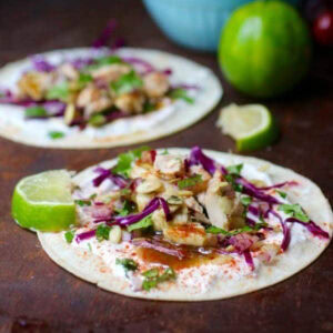 Two tuna tacos with limes on a plate.