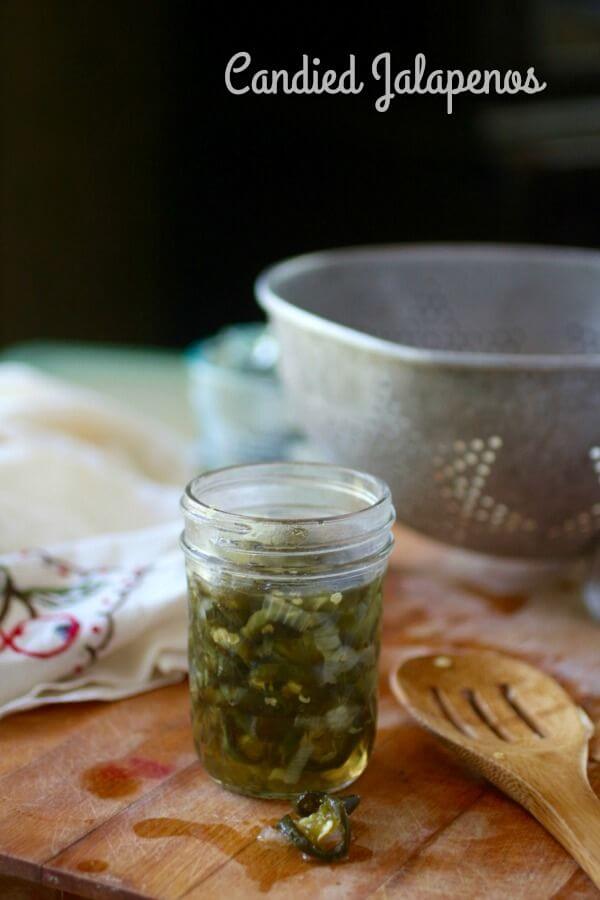 A small, open jar of jalapenos with a colander in the background.