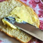A slice of white bread being spread with butter.