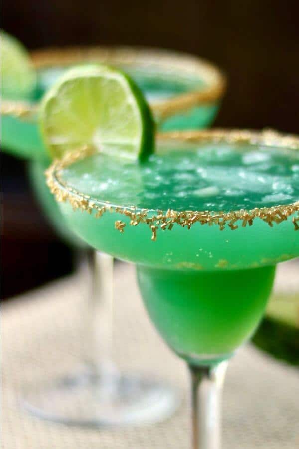 Closeup of a green margarita in a glass with gold sugar crystals.