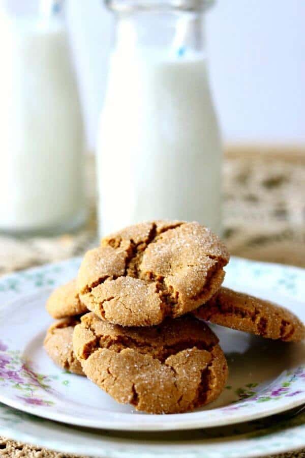 Peanut butter cookies stacked on a plate with glasses of milk in the background.