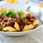 Chili over corn chip in a bowl.