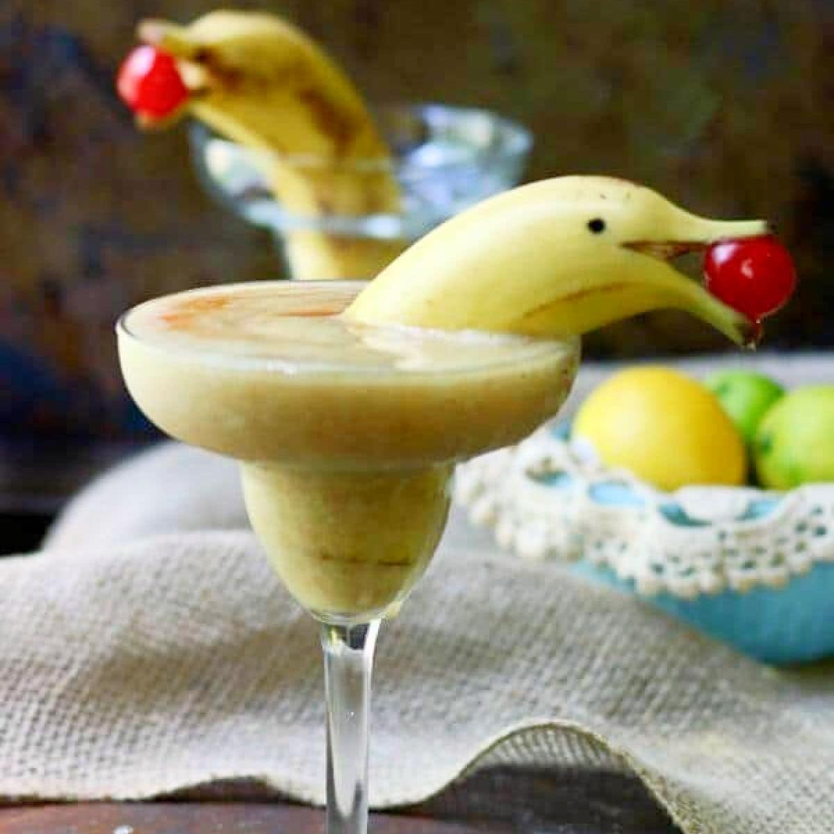 Closeup of two banana daiquiris garnished with bananas cut to look like dolphins.