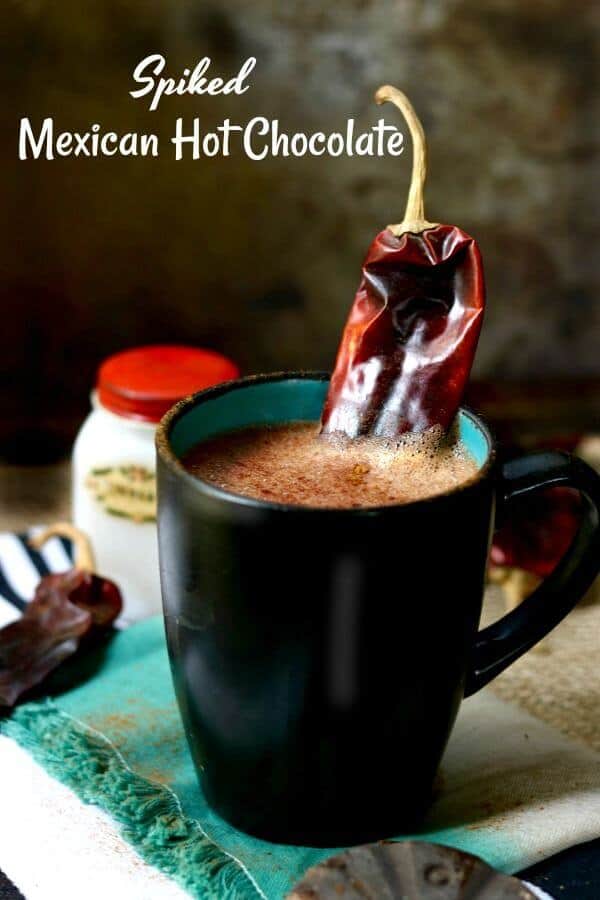 Spiked Mexican hot chocolate drink in a black mug with a bright teal interior. A dried chile is used for garnish.