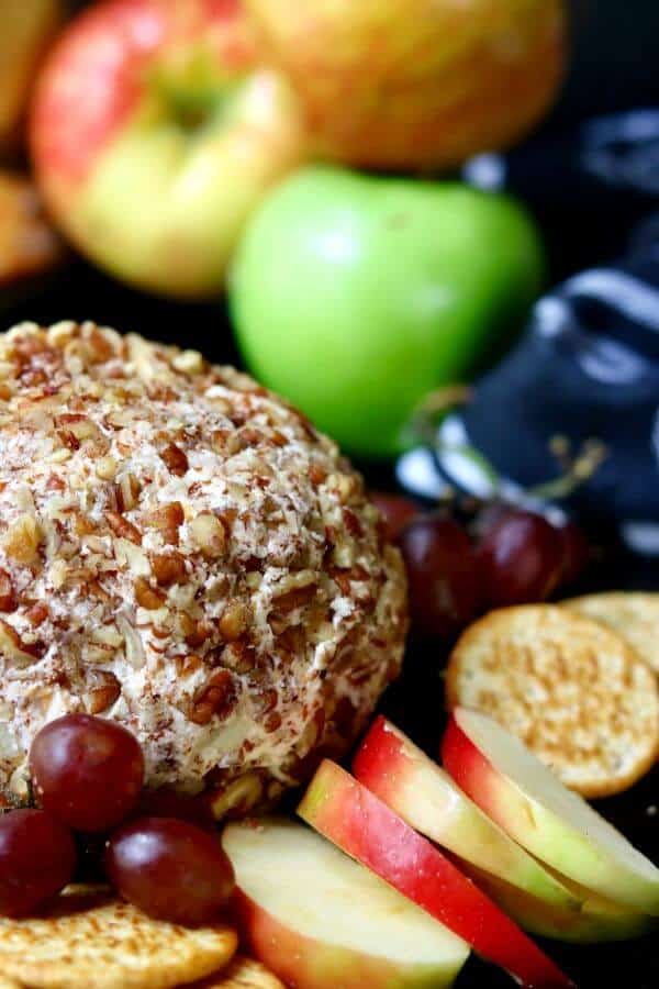 Close up of apple cheddar cheese ball with chopped pecans pressed into it to cover. Sliced apples to the side.