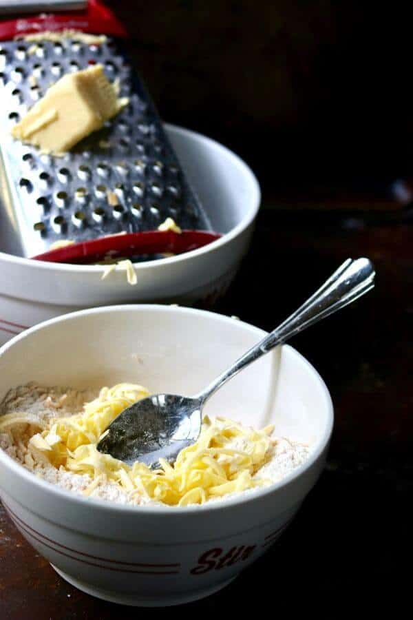 Cold butter is being grated into a bowl of flour 