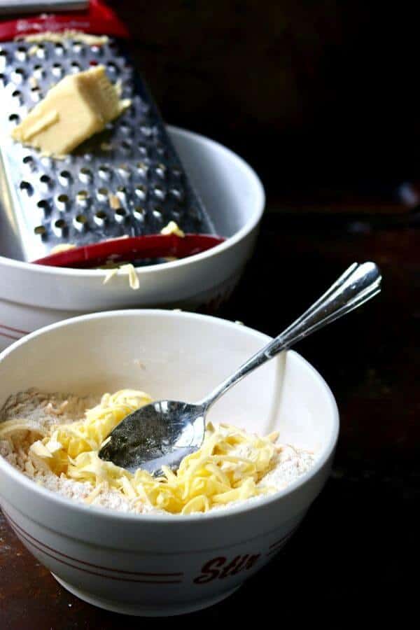 Cold butter is being grated into a bowl of flour