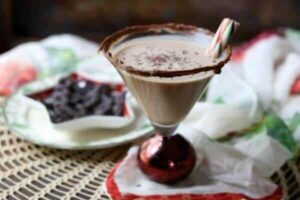 Chocolate peppermint martini in a red based martini glass is in the foreground with a star shaped dish of chocolate in the background.